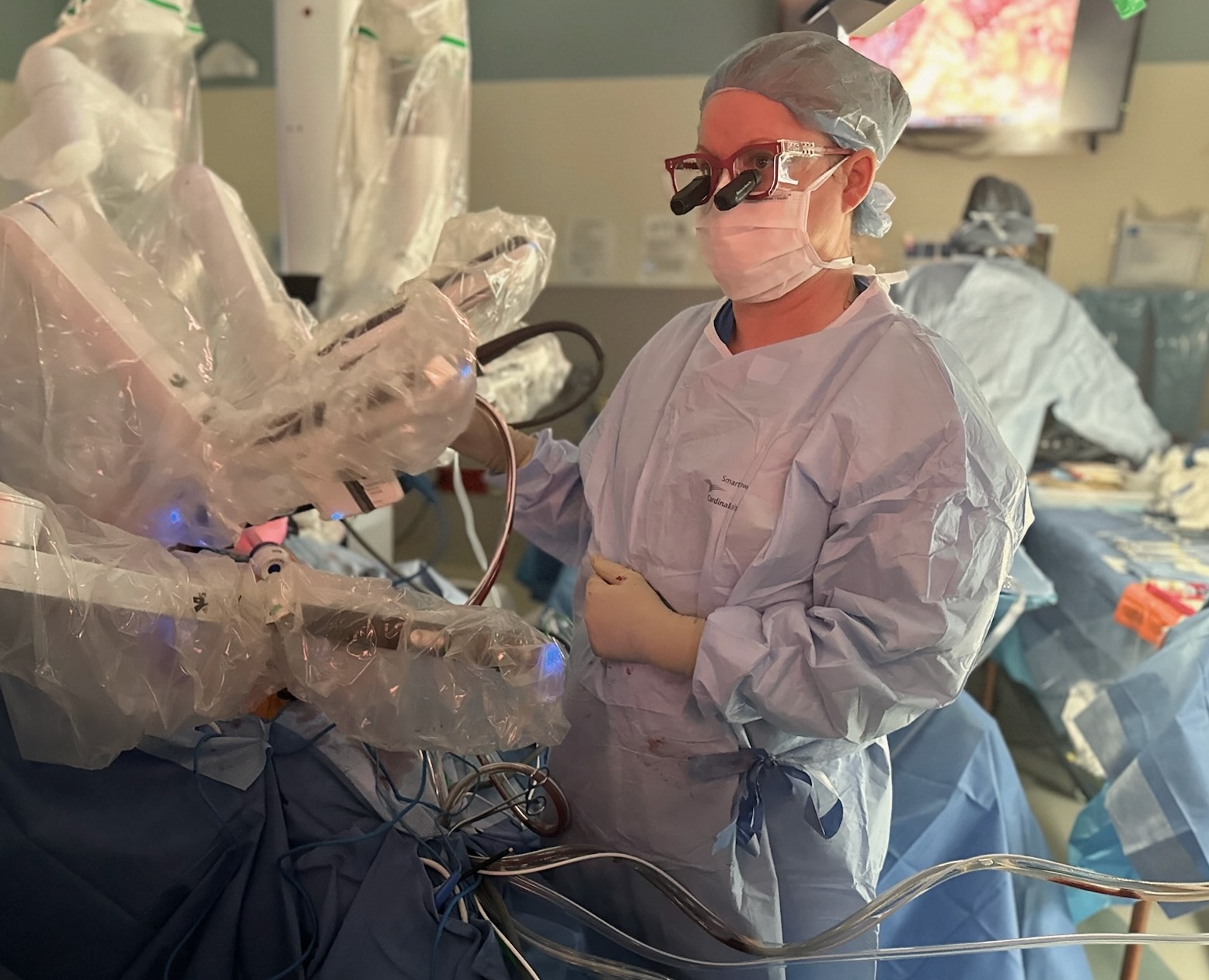 Surgeon in scrubs with red loupes standing next to a robotic platform